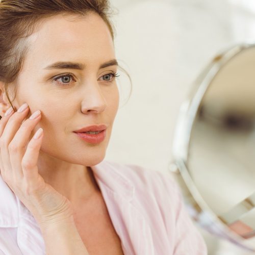 beautiful woman looking at her skin in mirror beautiful woman looking at her skin in mirror